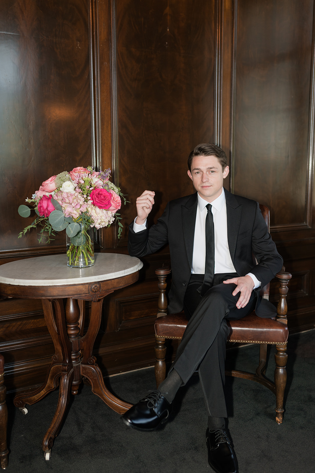 Groom seated portrait in a black suit in the wood paneled library at the Oklahoma Hall of Fame, Oklahoma wedding photographer