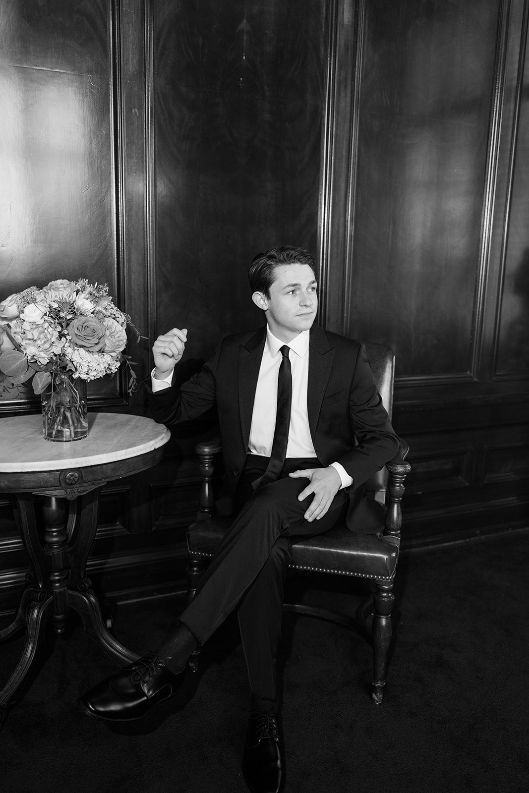 Black and white groom portrait seated in a leather chair at the Oklahoma Hall of Fame wedding venue in Oklahoma City