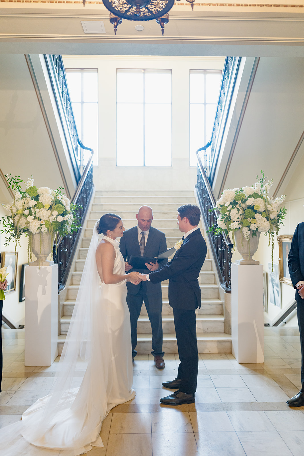 Bride and groom holding hands during their wedding ceremony in front of the grand staircase at the Oklahoma Hall of Fame in Oklahoma City