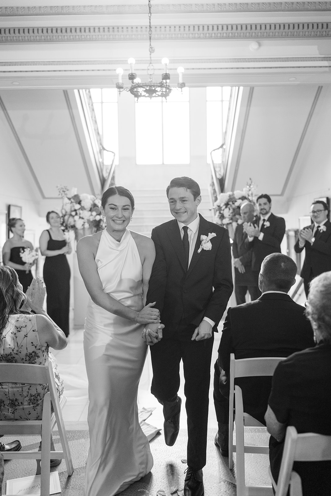 Black and white recessional photo of the newlyweds walking up the aisle hand in hand at the Oklahoma Hall of Fame, Oklahoma City